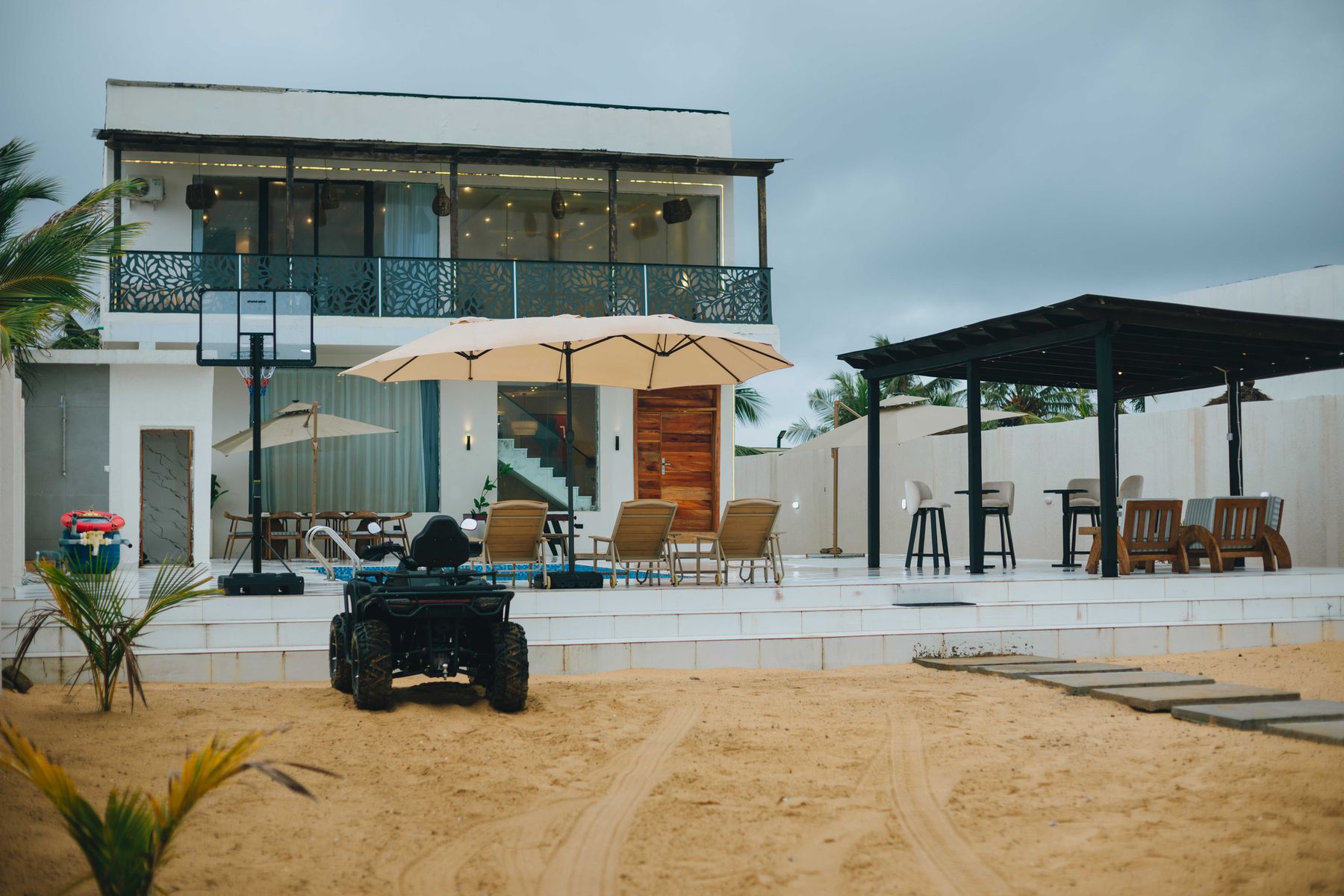 The villa from the sand, with parasols, loungers and a quad bike out front